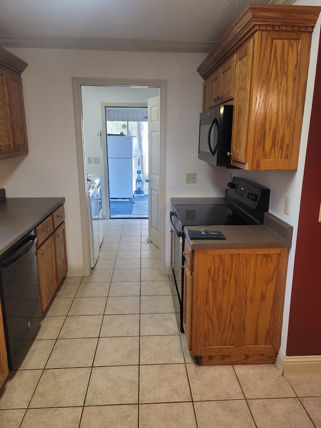 kitchen with dark countertops, black appliances, light tile patterned flooring, and brown cabinetry