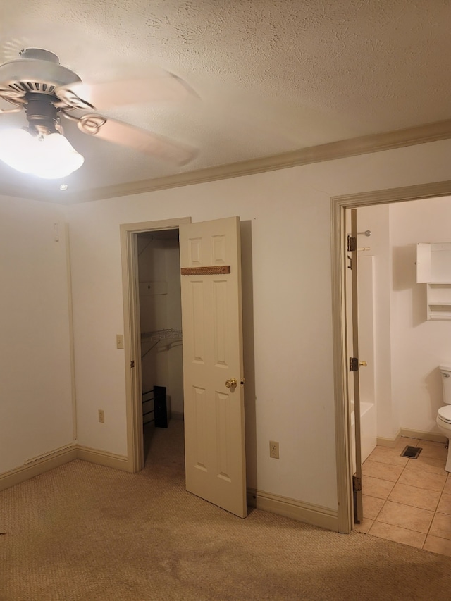 unfurnished bedroom with a walk in closet, a textured ceiling, light colored carpet, ceiling fan, and connected bathroom