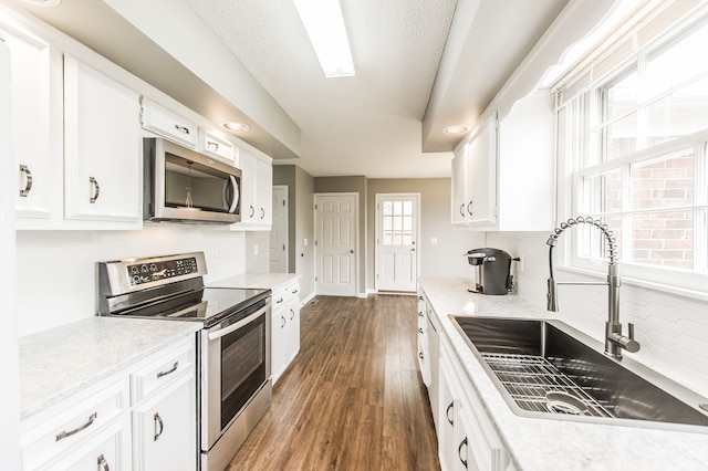 kitchen with sink, appliances with stainless steel finishes, dark hardwood / wood-style flooring, decorative backsplash, and white cabinets