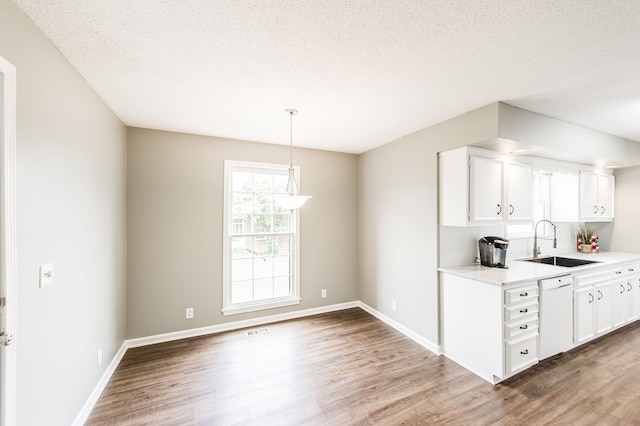 kitchen featuring sink, hardwood / wood-style floors, hanging light fixtures, white dishwasher, and white cabinets