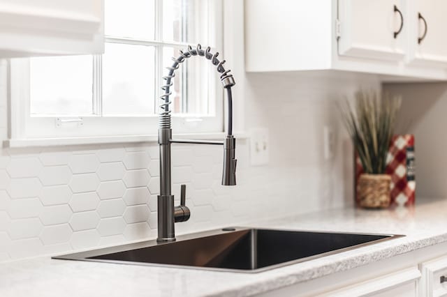 interior details with tasteful backsplash, sink, and white cabinets