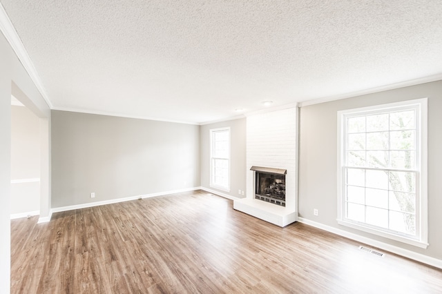 unfurnished living room with crown molding, a textured ceiling, a fireplace, and light hardwood / wood-style flooring