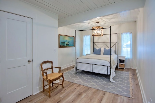 bedroom with hardwood / wood-style flooring, beamed ceiling, and an inviting chandelier