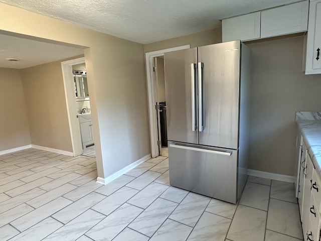 kitchen featuring stainless steel fridge, white cabinetry, and a textured ceiling