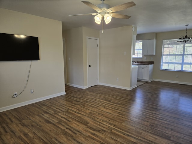 unfurnished living room with dark wood-type flooring and ceiling fan with notable chandelier