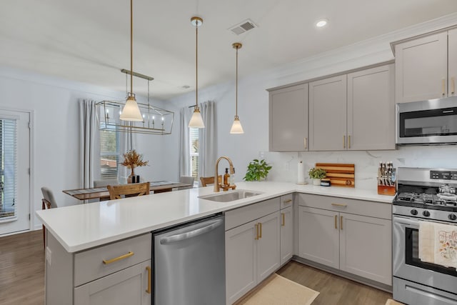 kitchen featuring stainless steel appliances, sink, kitchen peninsula, and decorative light fixtures