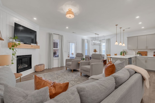 living room with light hardwood / wood-style flooring, ornamental molding, sink, a chandelier, and a fireplace