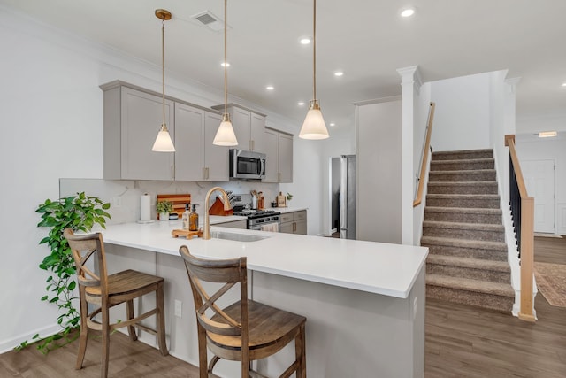 kitchen with a kitchen bar, appliances with stainless steel finishes, kitchen peninsula, and wood-type flooring