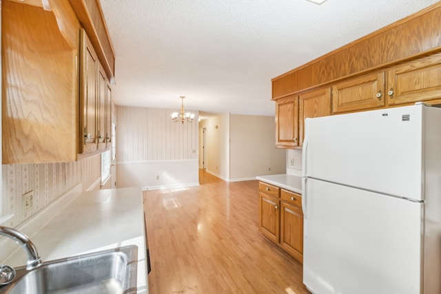 kitchen with white refrigerator, a notable chandelier, pendant lighting, sink, and light hardwood / wood-style flooring