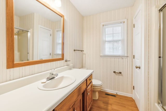 bathroom featuring wood-type flooring, vanity, toilet, and a shower with shower door