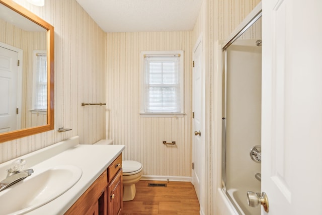 full bathroom with a textured ceiling, combined bath / shower with glass door, hardwood / wood-style floors, vanity, and toilet