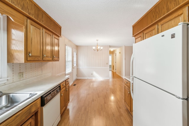 kitchen featuring hanging light fixtures, sink, a notable chandelier, light wood-type flooring, and white appliances