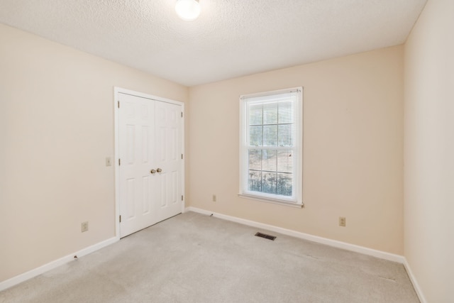 unfurnished room featuring a textured ceiling and light carpet