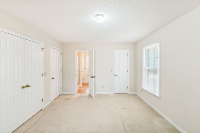 unfurnished bedroom featuring a textured ceiling, multiple closets, and light carpet