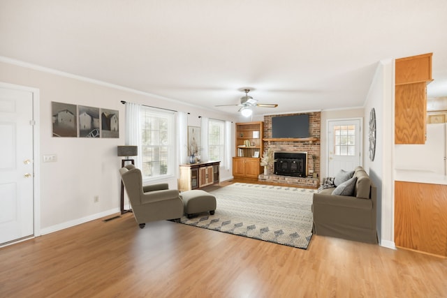 living room with light wood-type flooring, ceiling fan, ornamental molding, and a brick fireplace