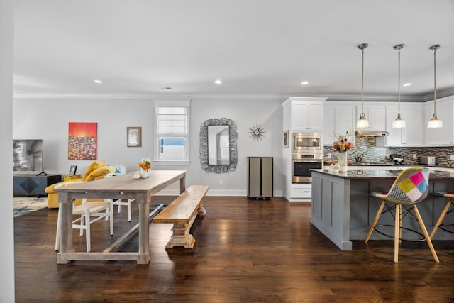 kitchen featuring dark hardwood / wood-style floors, a kitchen breakfast bar, hanging light fixtures, stainless steel appliances, and white cabinets