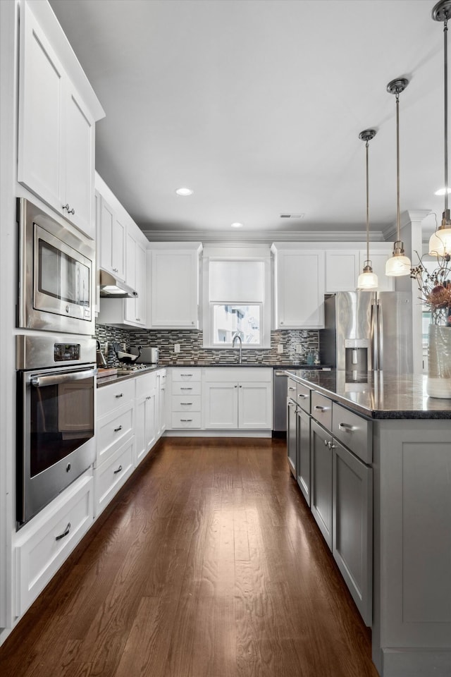 kitchen featuring dark wood-type flooring, stainless steel appliances, dark stone counters, pendant lighting, and white cabinets