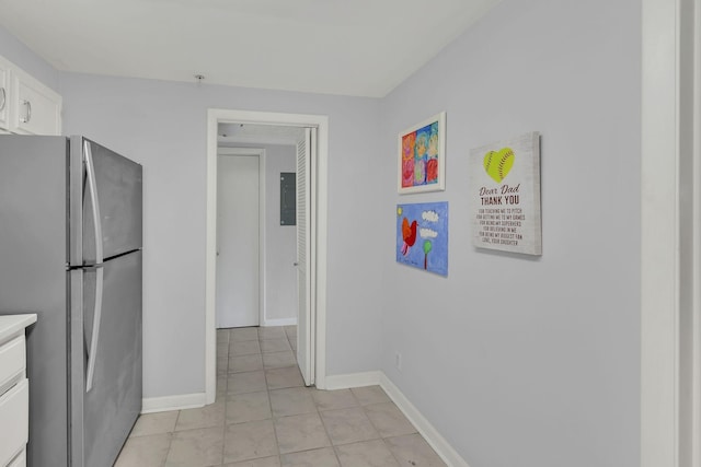 kitchen featuring freestanding refrigerator, white cabinets, light tile patterned flooring, and baseboards