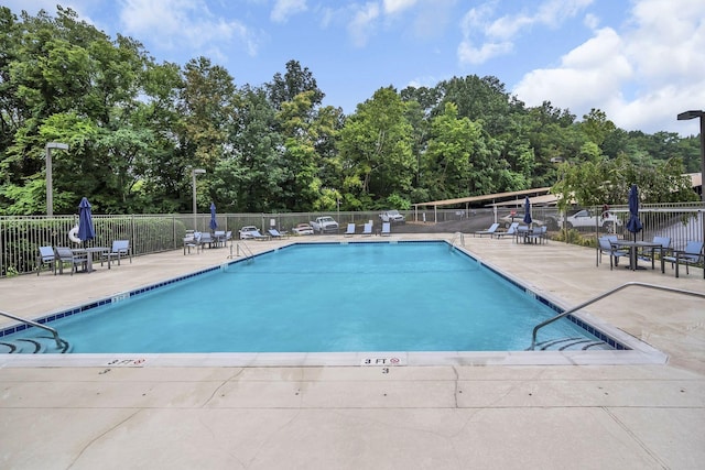 community pool with fence, a patio area, and view of scattered trees