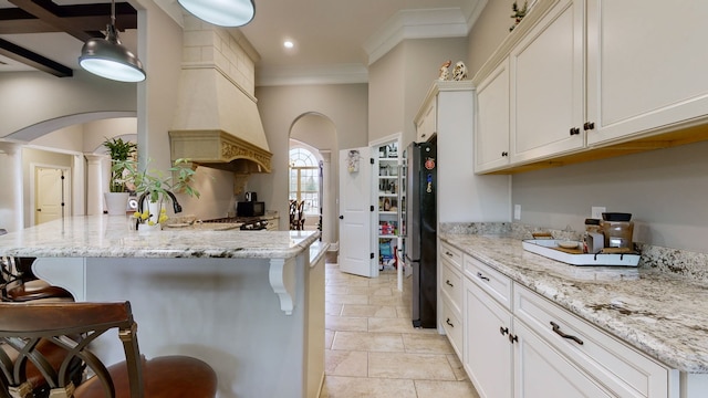 kitchen featuring white cabinets, light stone countertops, a breakfast bar area, and stainless steel fridge