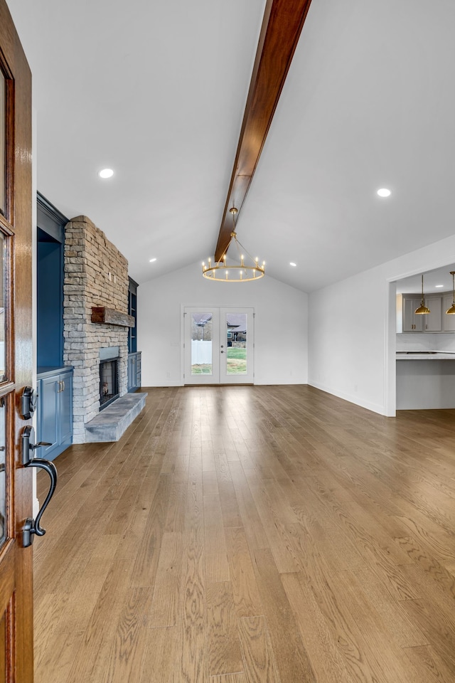 unfurnished living room featuring french doors, lofted ceiling with beams, a notable chandelier, a fireplace, and light hardwood / wood-style floors