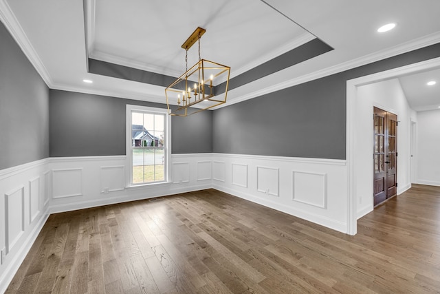 unfurnished dining area with a tray ceiling, crown molding, wood-type flooring, and a chandelier