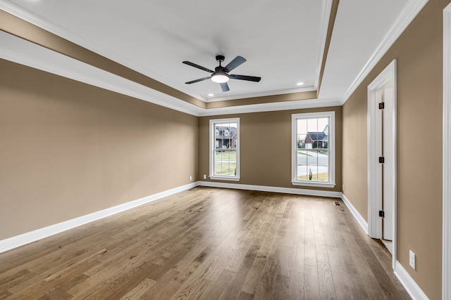 empty room with crown molding, hardwood / wood-style flooring, a tray ceiling, and ceiling fan