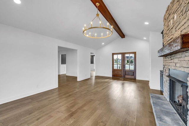 unfurnished living room with french doors, lofted ceiling with beams, a stone fireplace, hardwood / wood-style floors, and a notable chandelier