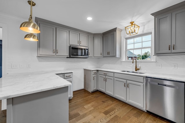 kitchen featuring wood-type flooring, appliances with stainless steel finishes, sink, pendant lighting, and ornamental molding