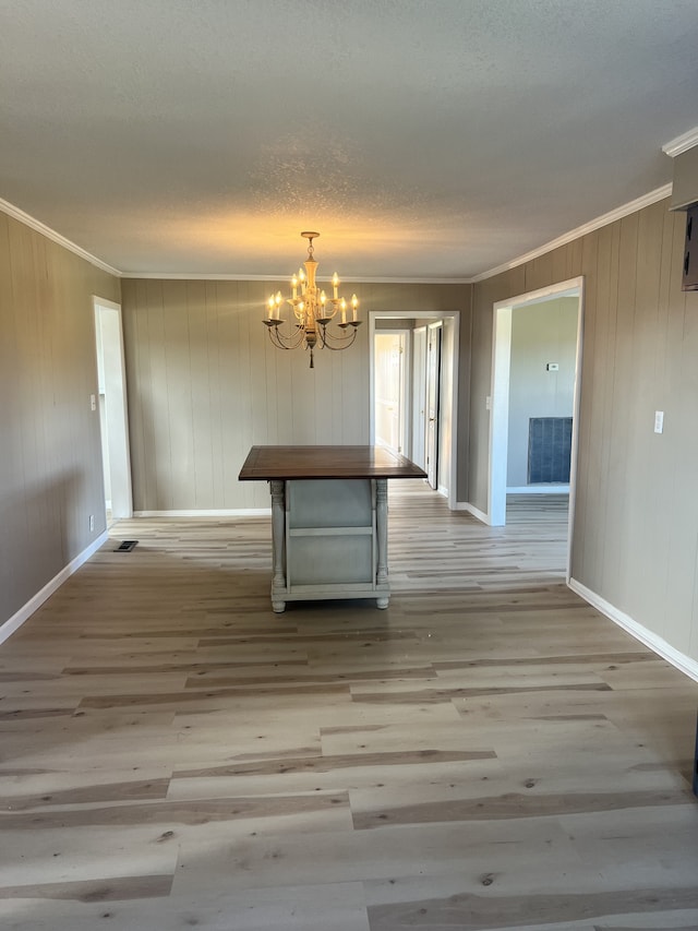 unfurnished dining area featuring wooden walls, ornamental molding, an inviting chandelier, light wood-type flooring, and a textured ceiling