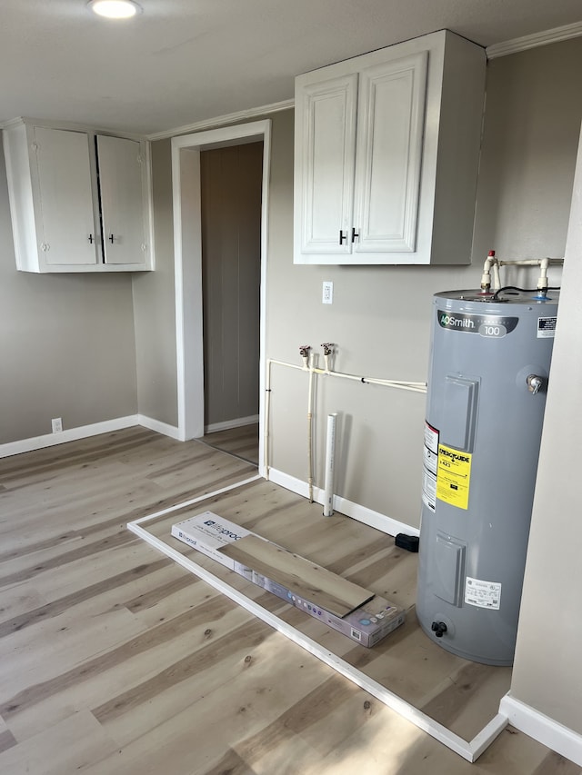 clothes washing area featuring electric water heater, cabinets, light wood-type flooring, and ornamental molding