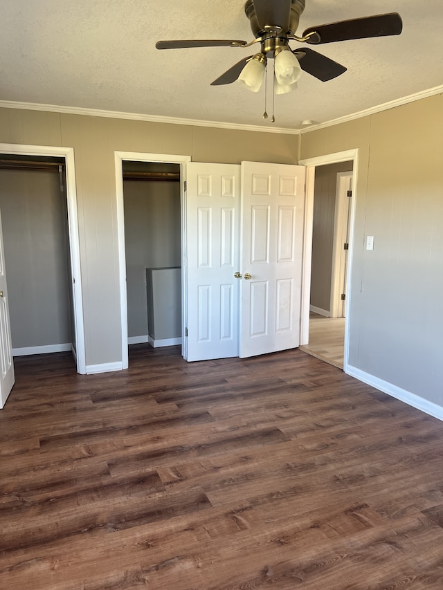 unfurnished bedroom featuring multiple closets, dark wood-type flooring, crown molding, and ceiling fan