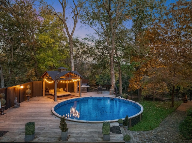 pool at dusk featuring a wooden deck and area for grilling