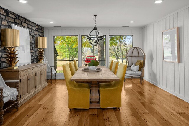 dining space with light hardwood / wood-style floors, wood walls, and an inviting chandelier