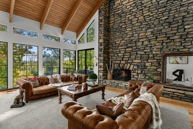 living room with hardwood / wood-style floors, beam ceiling, high vaulted ceiling, wooden ceiling, and a stone fireplace