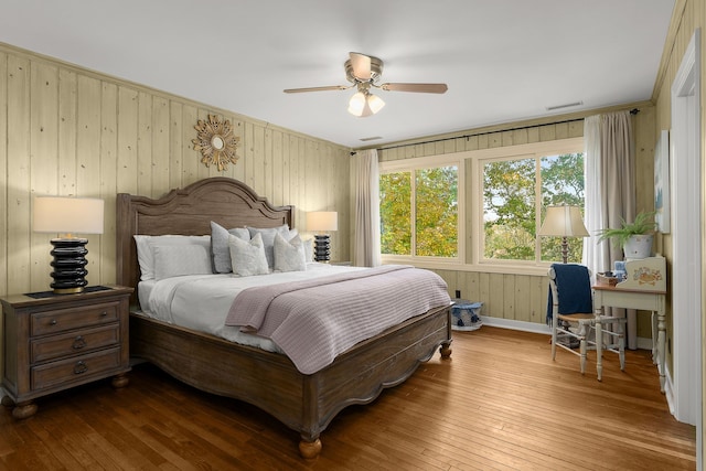 bedroom with wood walls, hardwood / wood-style floors, and ceiling fan