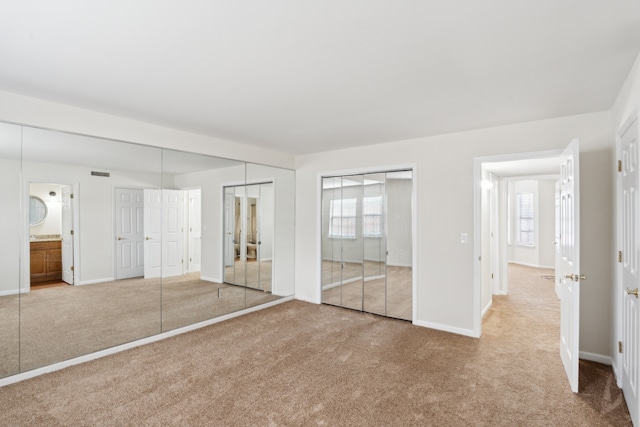 unfurnished bedroom with multiple windows, carpet floors, ensuite bath, and two closets