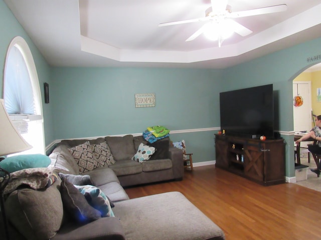 living room featuring wood-type flooring, a tray ceiling, and ceiling fan