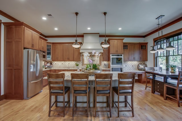 kitchen featuring pendant lighting, custom exhaust hood, a center island, appliances with stainless steel finishes, and light hardwood / wood-style floors