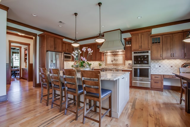 kitchen with pendant lighting, a center island, light hardwood / wood-style floors, light stone counters, and stainless steel appliances