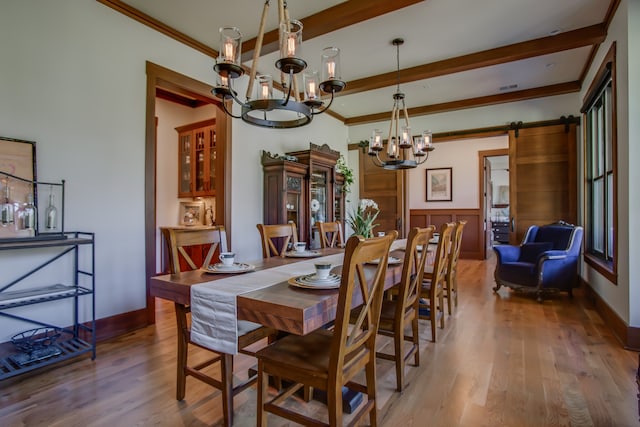 dining area with beam ceiling, an inviting chandelier, a barn door, hardwood / wood-style flooring, and ornamental molding