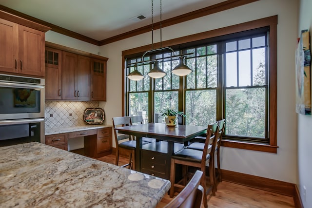 kitchen with light stone countertops, hanging light fixtures, stainless steel double oven, backsplash, and ornamental molding