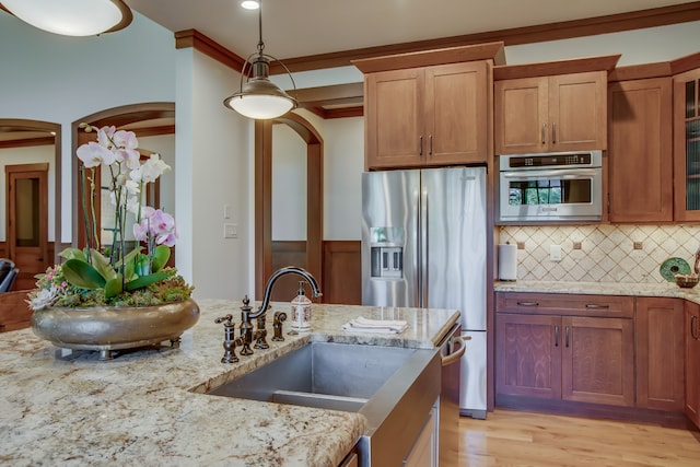 kitchen with sink, ornamental molding, decorative light fixtures, light stone counters, and stainless steel appliances