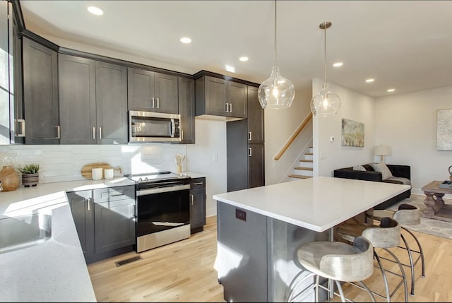 kitchen featuring tasteful backsplash, a kitchen island, hanging light fixtures, light hardwood / wood-style floors, and stainless steel appliances