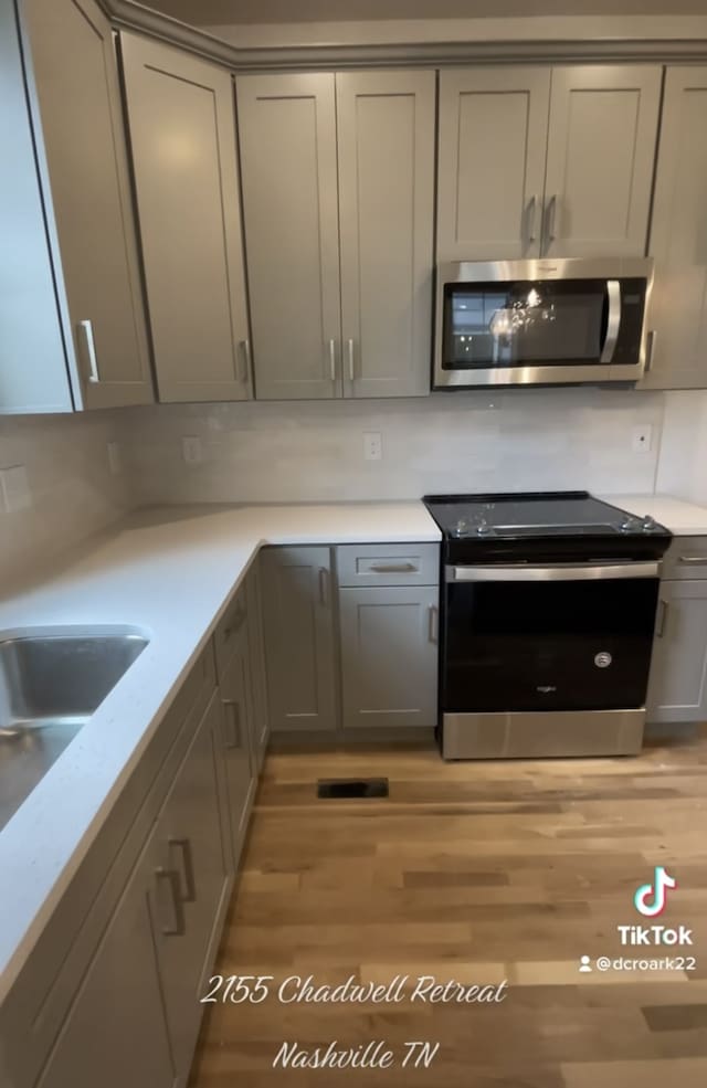 kitchen featuring light stone counters, stainless steel appliances, light wood-type flooring, and gray cabinets