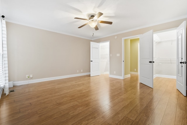 unfurnished bedroom featuring light hardwood / wood-style floors, ornamental molding, ceiling fan, a spacious closet, and a closet