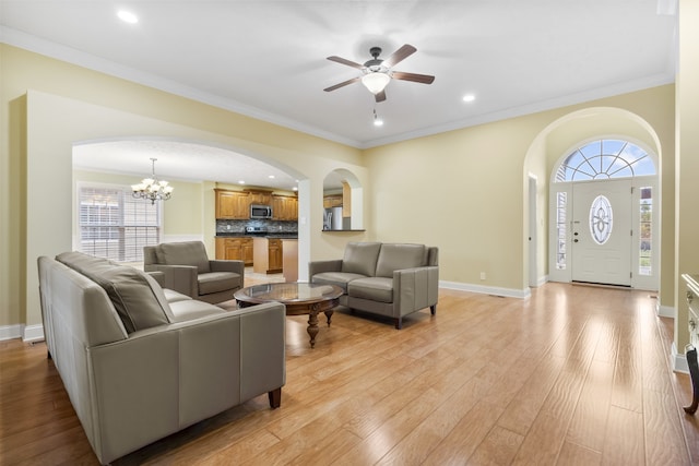 living room featuring ornamental molding, ceiling fan with notable chandelier, light hardwood / wood-style flooring, and a healthy amount of sunlight