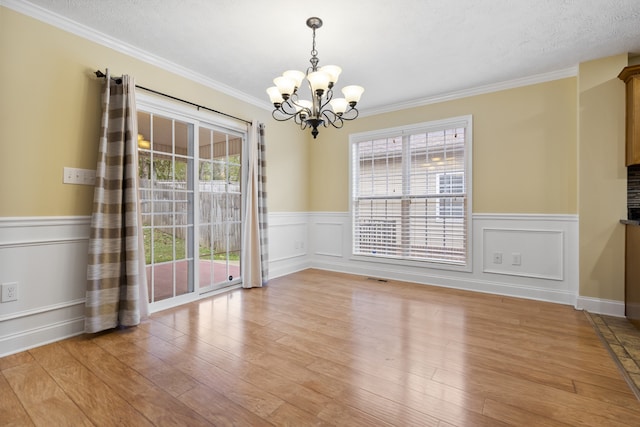 unfurnished dining area with an inviting chandelier, a textured ceiling, light wood-type flooring, and crown molding