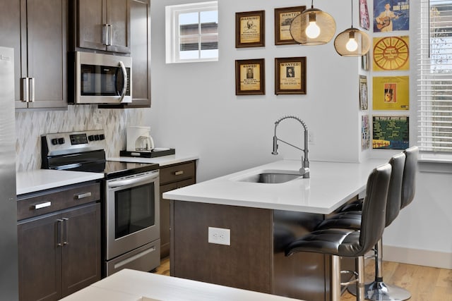 kitchen with sink, a breakfast bar area, stainless steel appliances, decorative light fixtures, and light hardwood / wood-style flooring