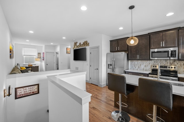 kitchen with a breakfast bar area, dark brown cabinets, stainless steel appliances, decorative light fixtures, and light wood-type flooring